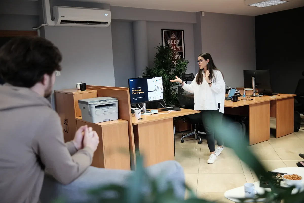 Presenting work on a monitor to a colleague in an open-plan office.